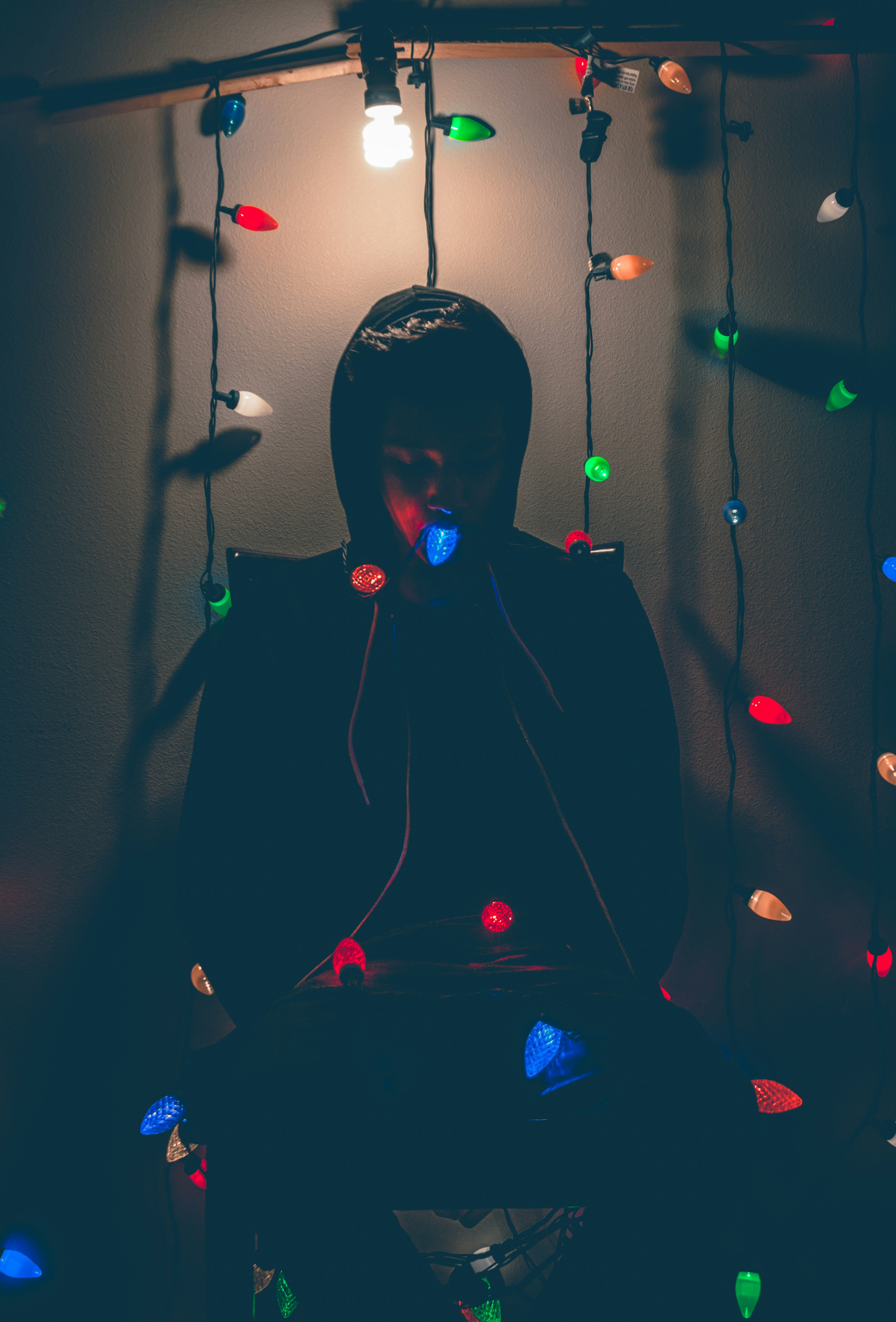 man sitting while biting multicolored string lights